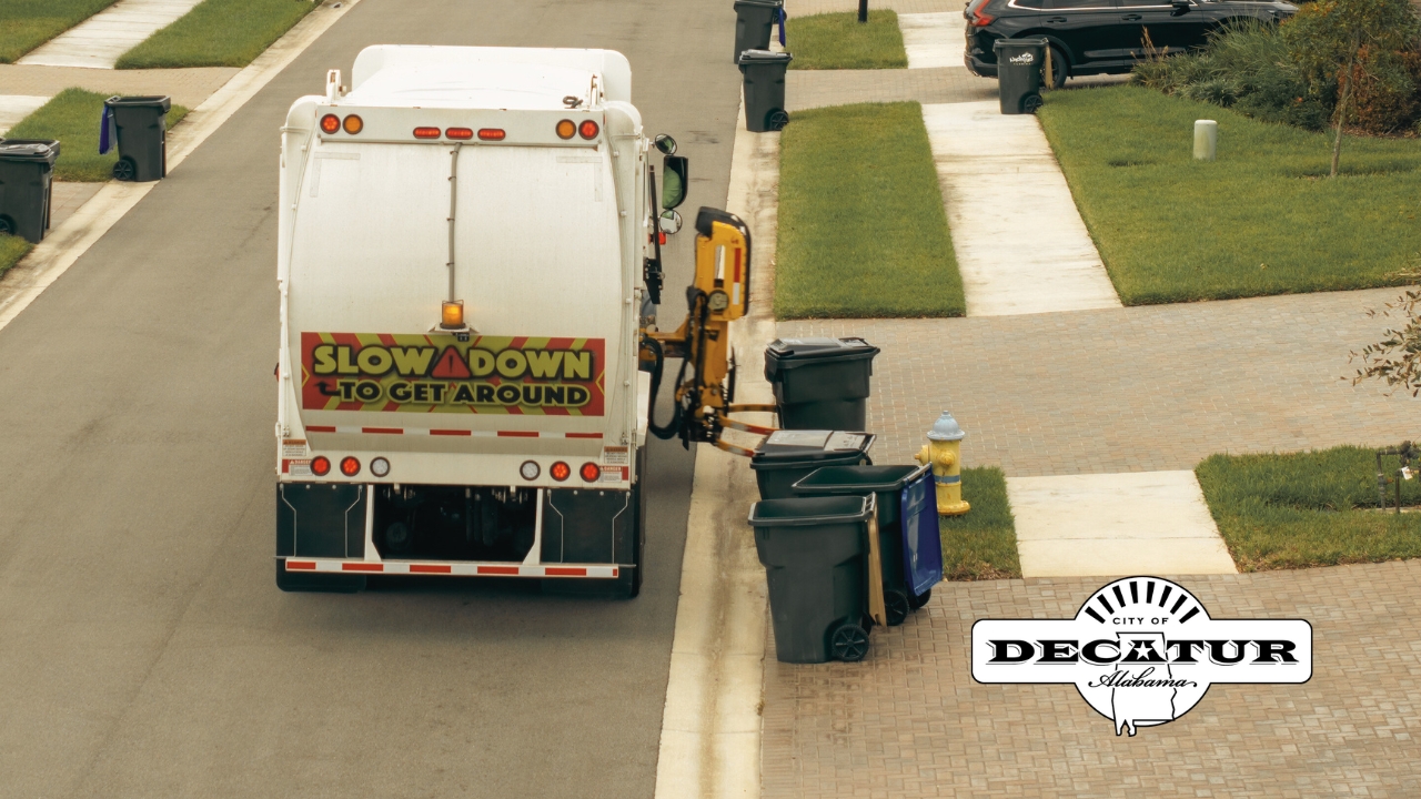 A garbage truck makes its way through a neighborhood emptying garbage cans