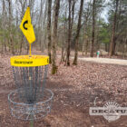 A disc golf basket at the Flying Dragon Disc Golf course is now adorned with yellow trim and a yellow hole number flag.