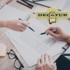 a stock picture of two hands that are holding pens and pointed at a piece of paper.