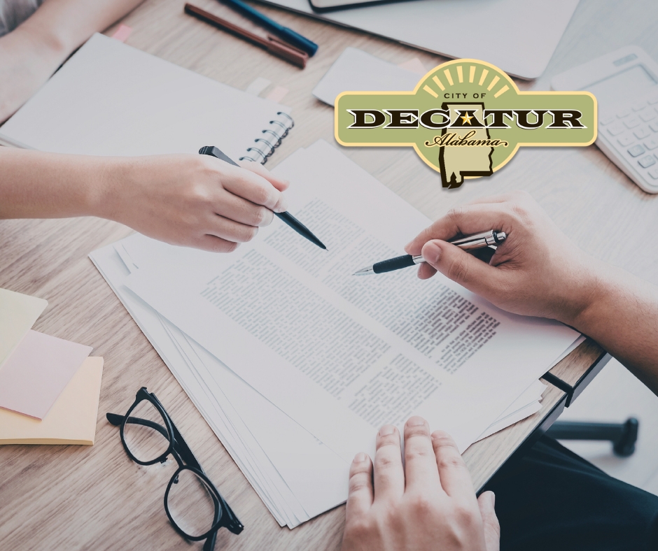 a stock picture of two hands that are holding pens and pointed at a piece of paper.